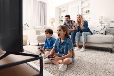 Photo of Cute kids playing video games while their parents resting on sofa indoors