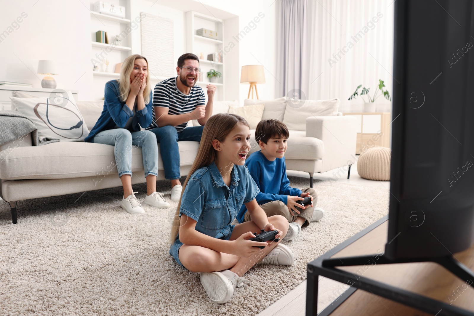 Photo of Cute kids playing video games while their parents resting on sofa indoors