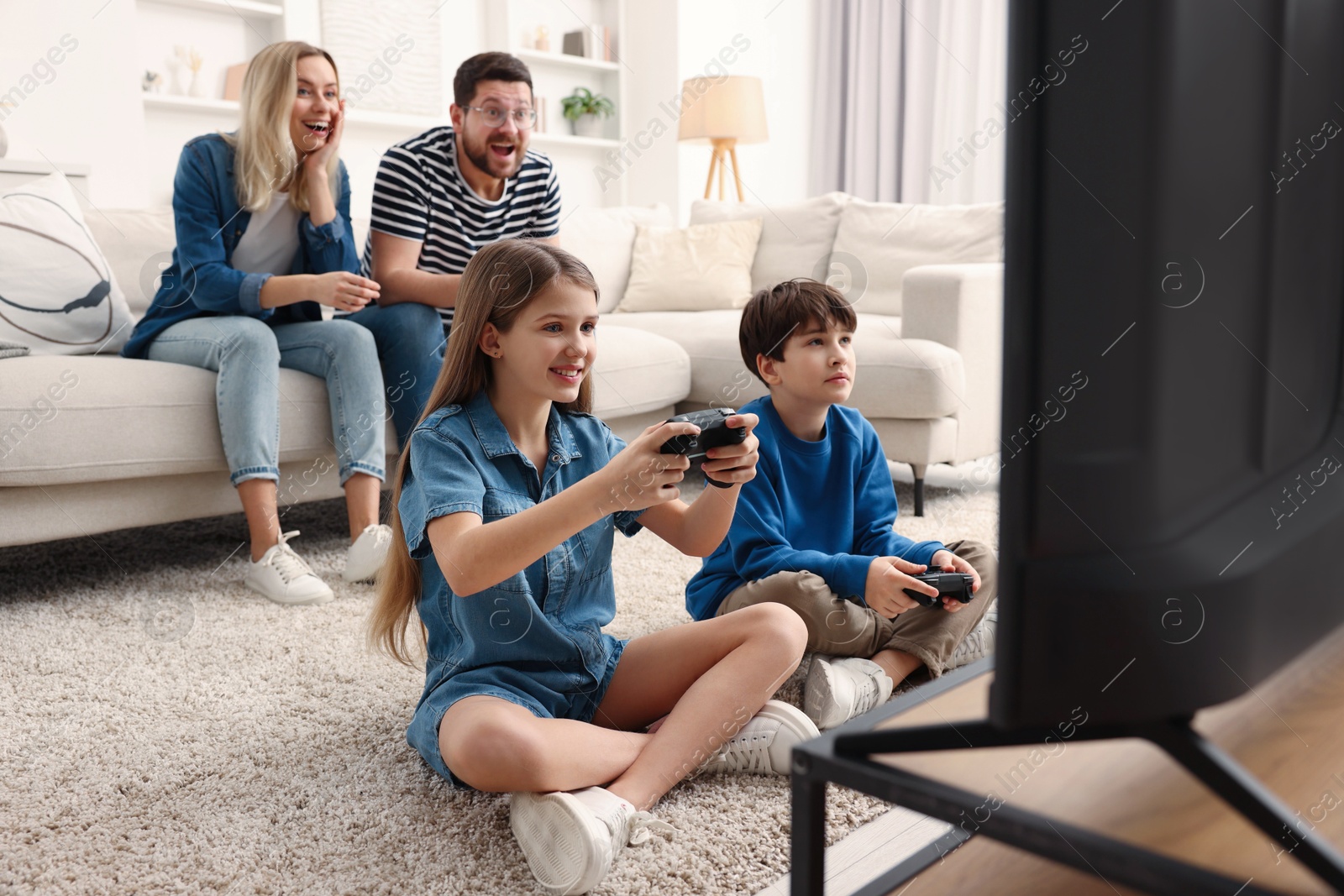 Photo of Cute kids playing video games while their parents resting on sofa indoors