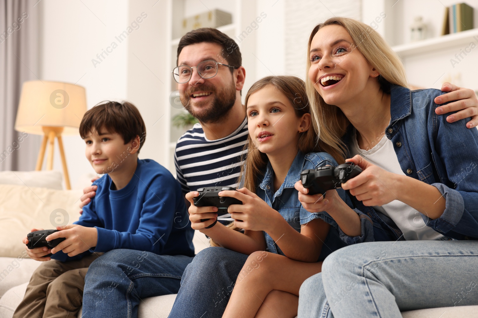 Photo of Happy family playing video games on sofa in living room