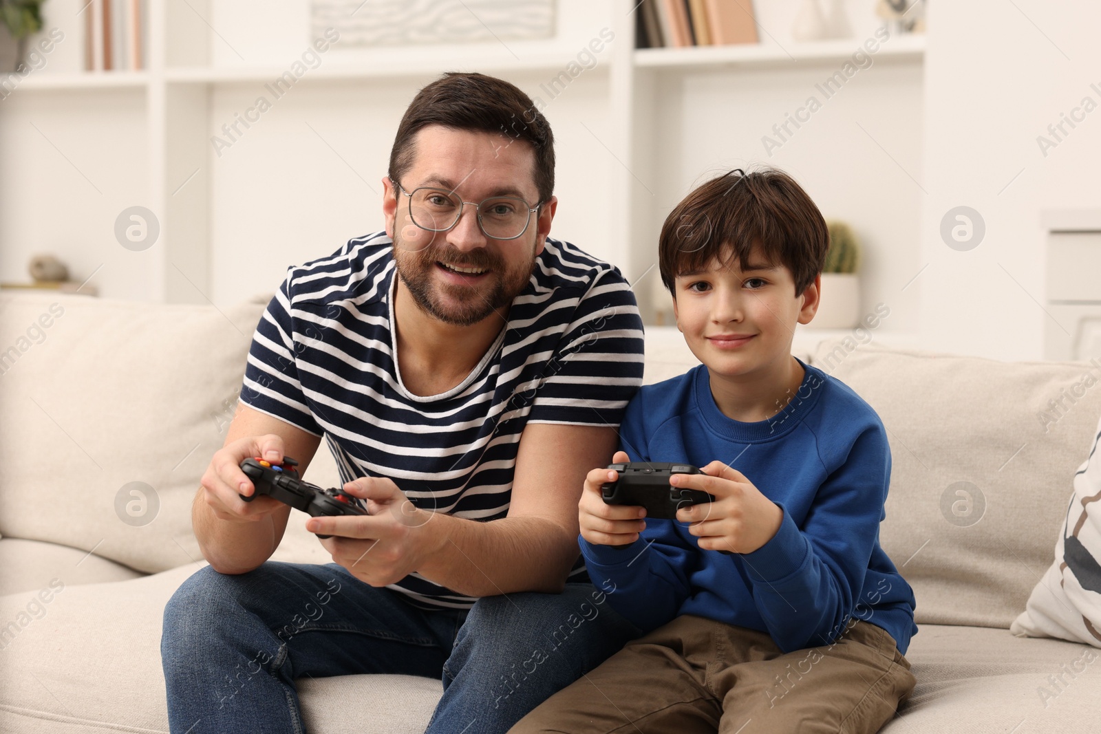 Photo of Father and his son playing video games on sofa in living room