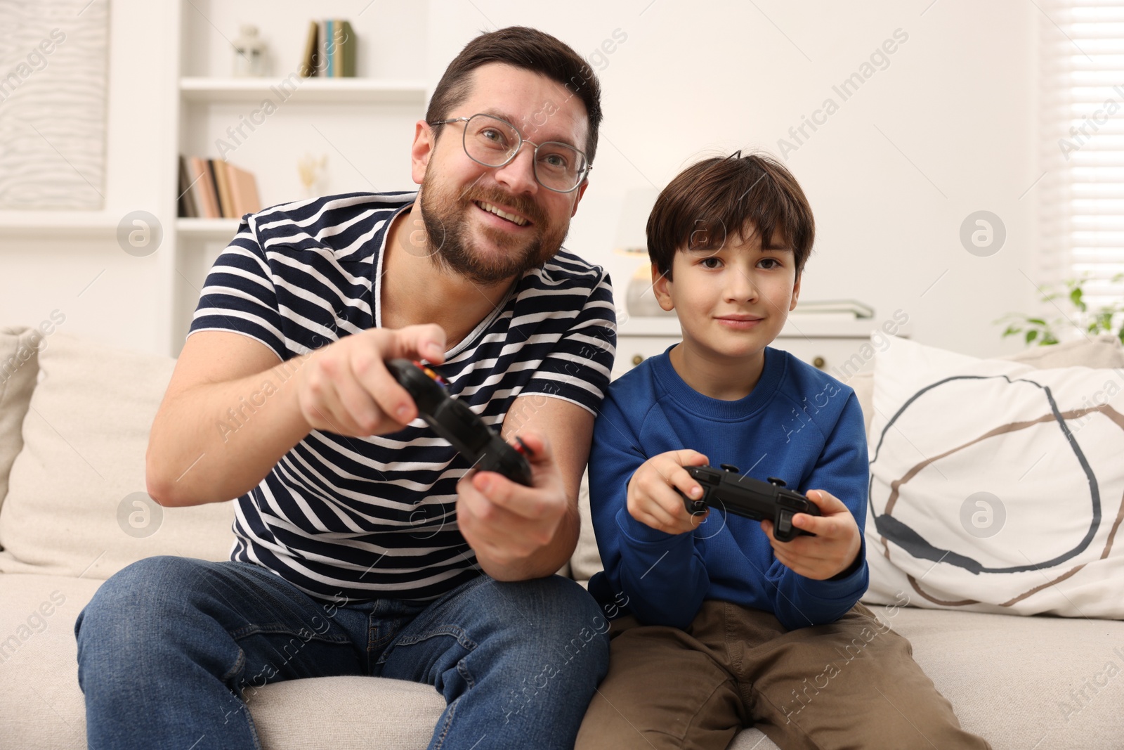 Photo of Father and his son playing video games on sofa in living room