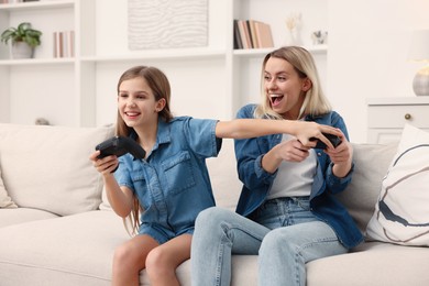 Photo of Happy mother and her daughter playing video games on sofa in living room