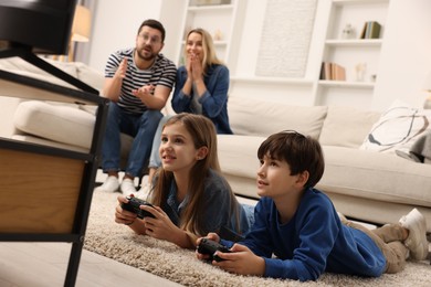 Photo of Cute kids playing video games while their parents resting on sofa at home, selective focus