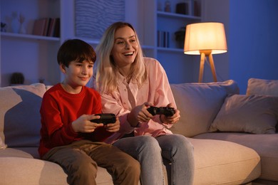 Photo of Happy mother and her son playing video games on sofa in living room