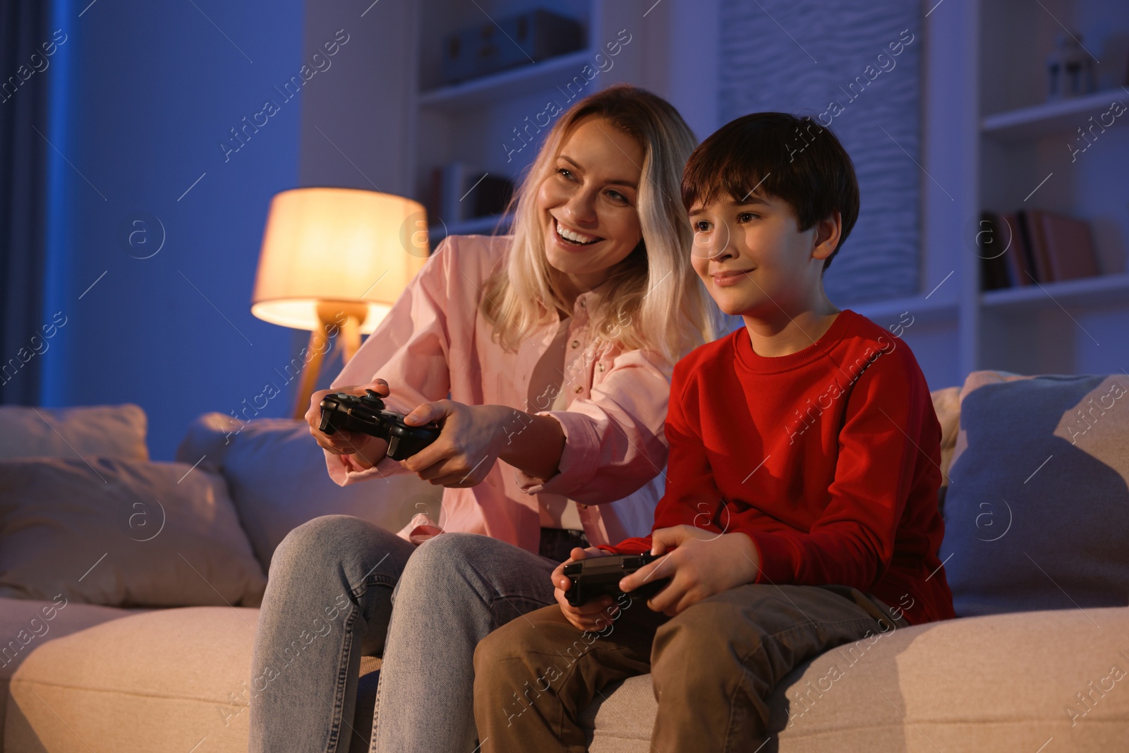 Photo of Happy mother and her son playing video games on sofa in living room