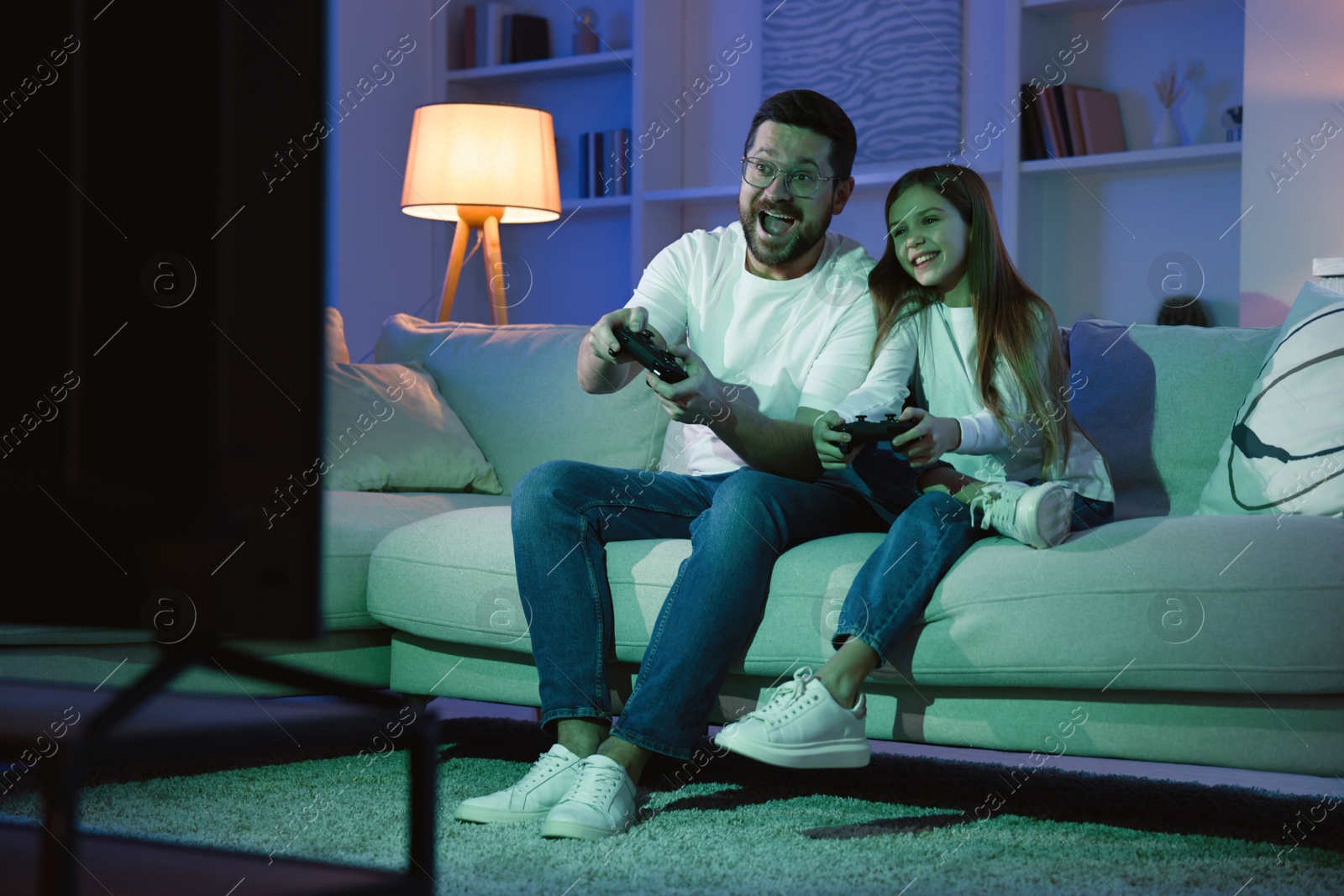 Photo of Happy father and his daughter playing video games on sofa in living room