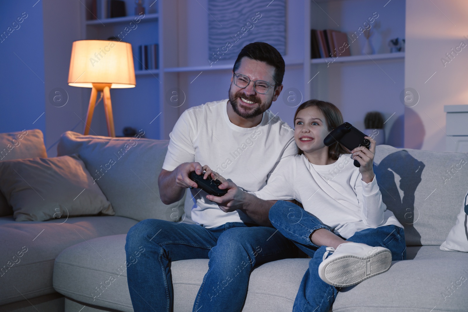 Photo of Happy father and his daughter playing video games on sofa in living room