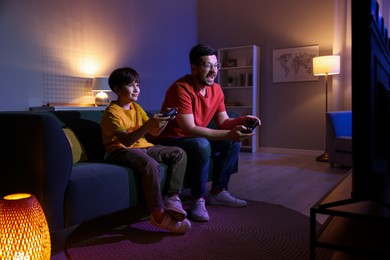 Photo of Happy father and his son playing video games on sofa in living room at night