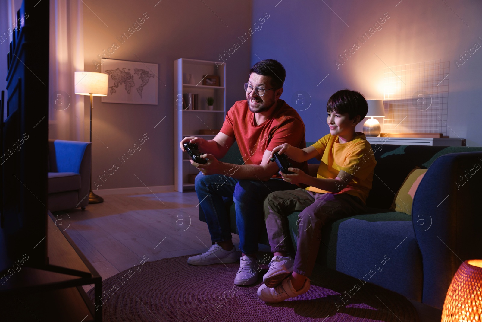 Photo of Happy father and his son playing video games on sofa in living room at night