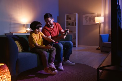 Photo of Happy father and his son playing video games on sofa in living room at night