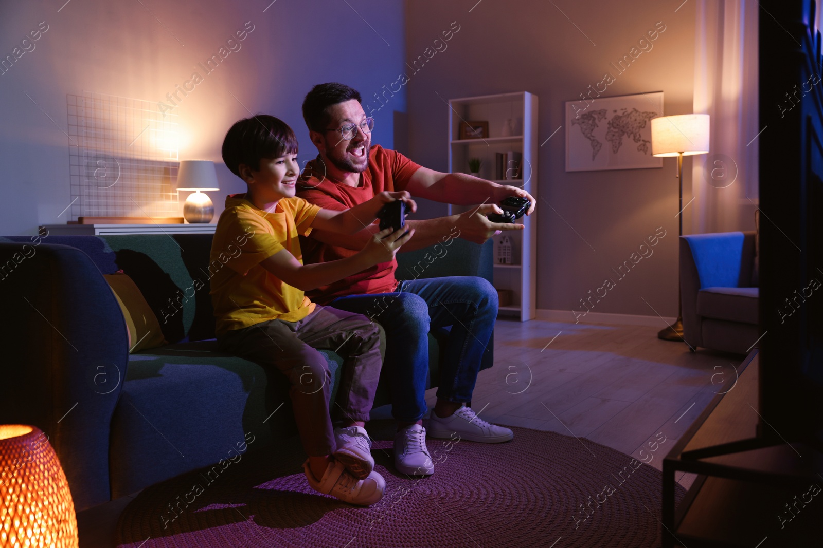 Photo of Happy father and his son playing video games on sofa in living room at night