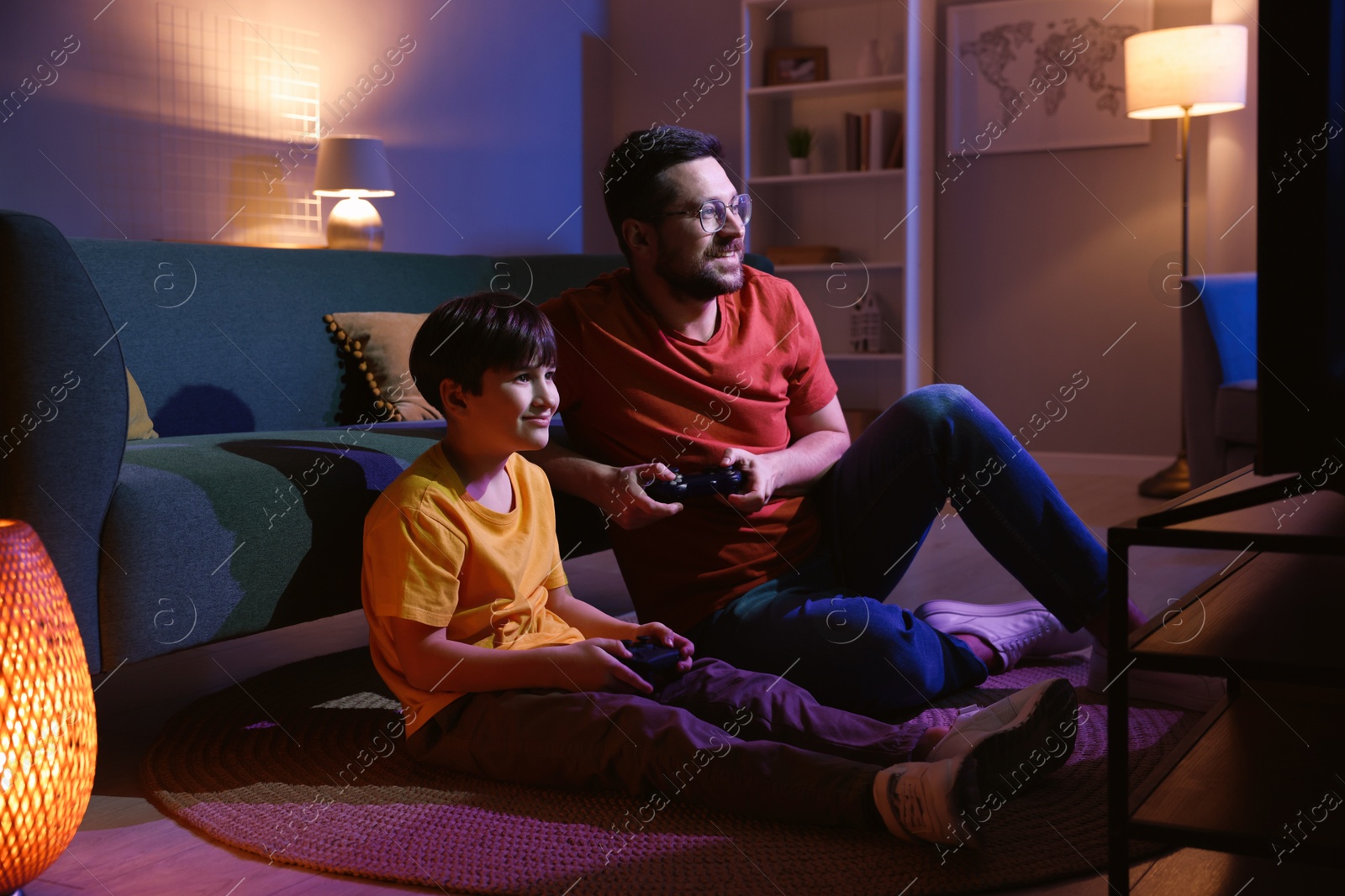 Photo of Happy father and his son playing video games on floor in living room at night