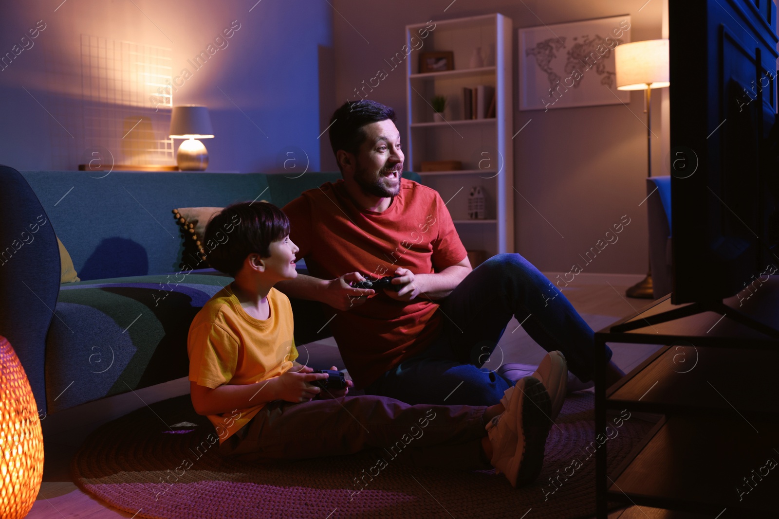 Photo of Happy father and his son playing video games on floor in living room at night