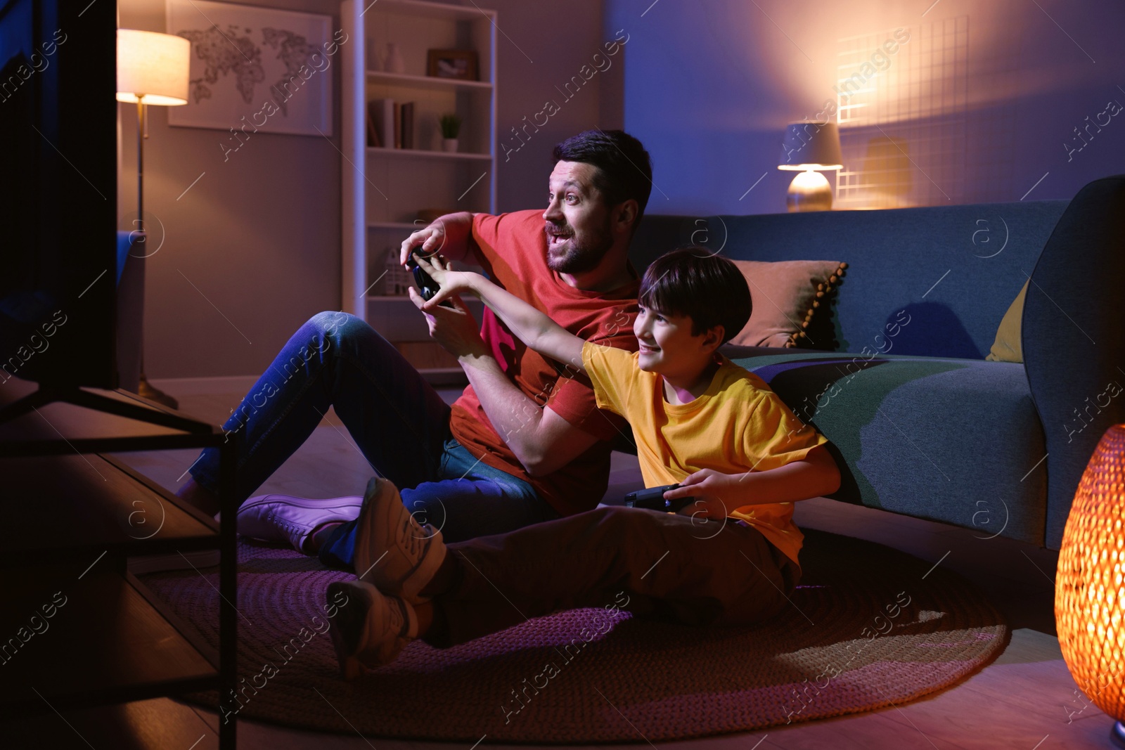 Photo of Happy father and his son playing video games on floor in living room at night