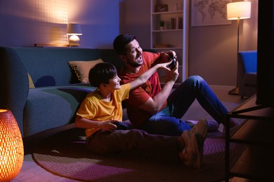 Photo of Happy father and his son playing video games on floor in living room at night