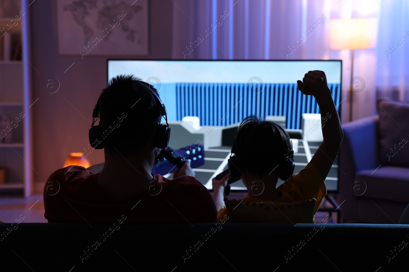 Photo of Father and his son playing video game on sofa in living room, back view