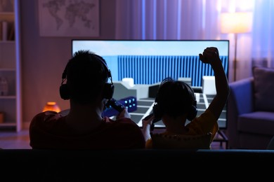 Photo of Father and his son playing video game on sofa in living room, back view