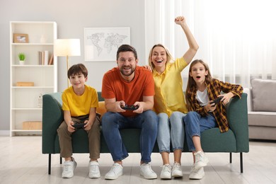 Photo of Happy family playing video games on sofa in living room