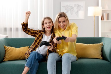 Photo of Happy mother and her daughter playing video games on sofa in living room