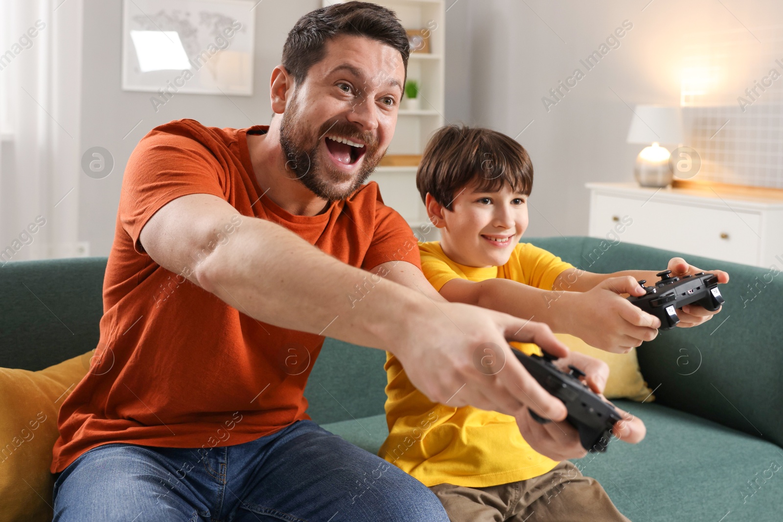 Photo of Happy father and his son playing video games on sofa in living room