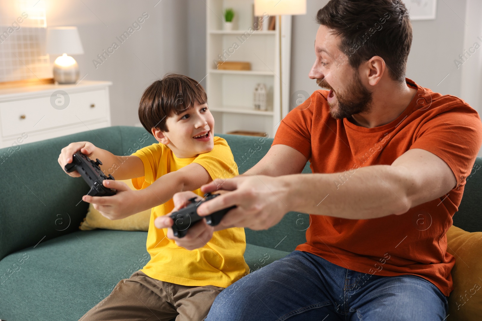 Photo of Happy father and his son playing video games on sofa in living room