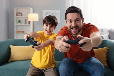 Photo of Happy father and his son playing video games on sofa in living room