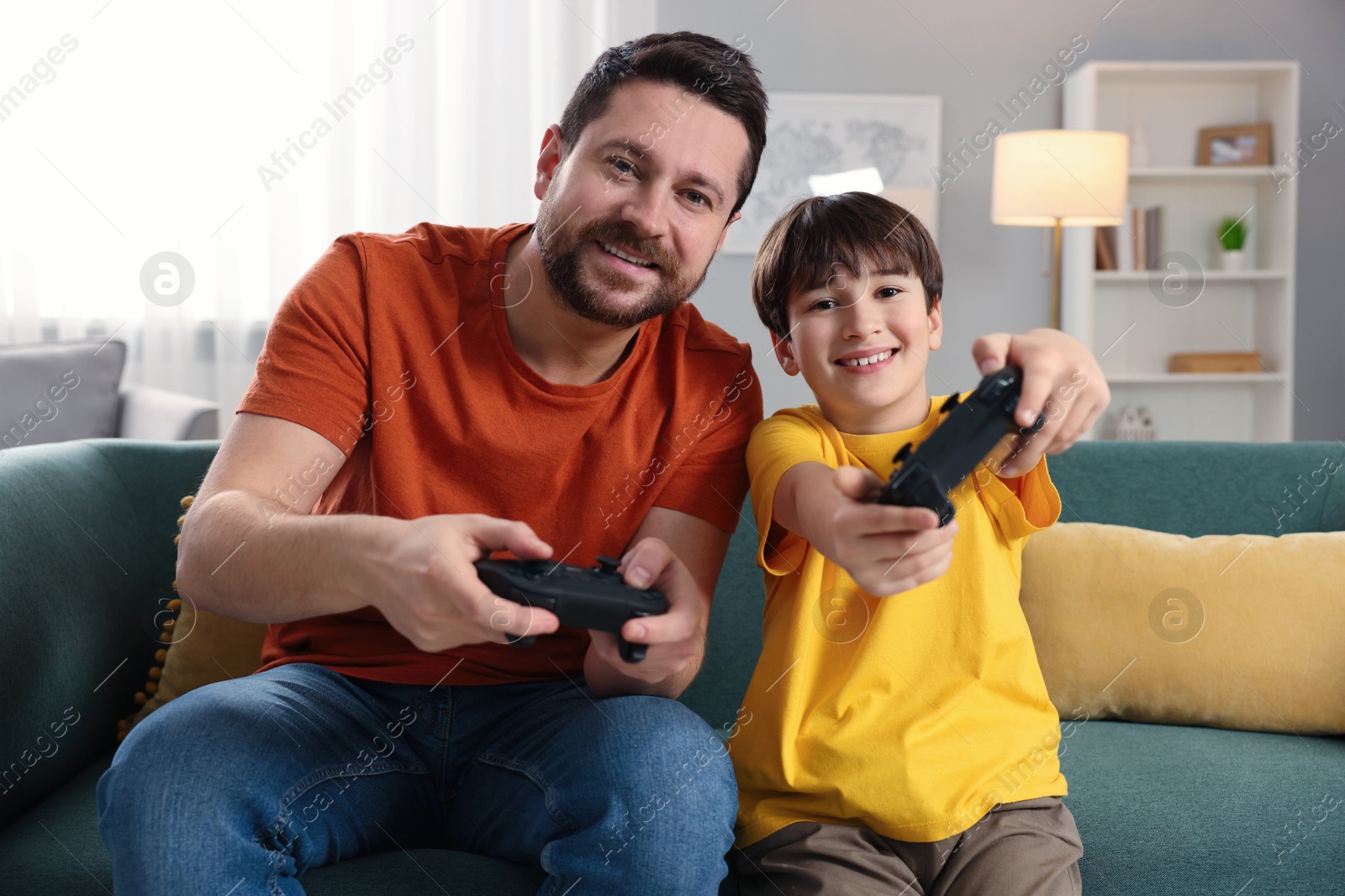 Photo of Happy father and his son playing video games on sofa in living room