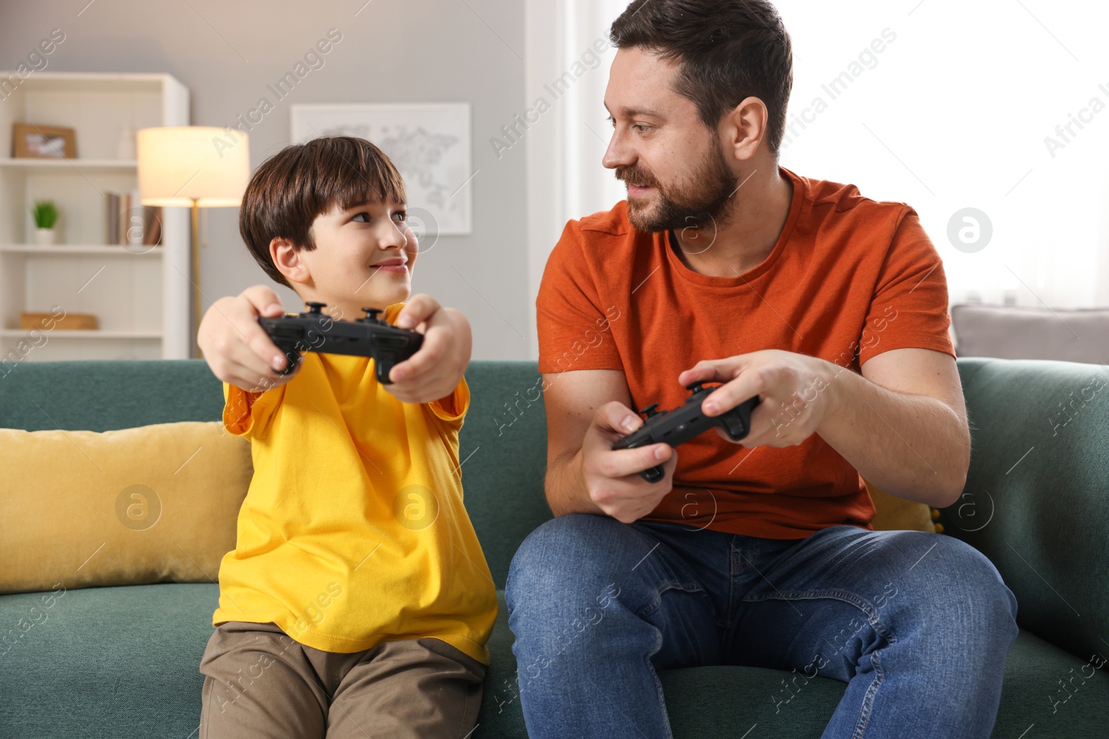 Photo of Happy father and his son playing video games on sofa in living room