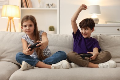 Photo of Cute kids playing video games on sofa in living room