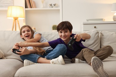 Photo of Cute kids playing video games on sofa in living room