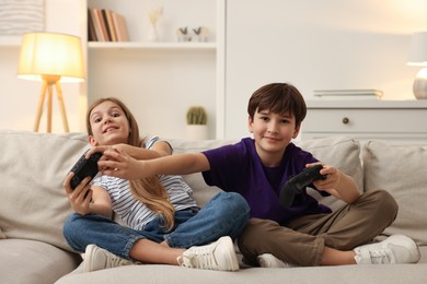 Photo of Cute kids playing video games on sofa in living room