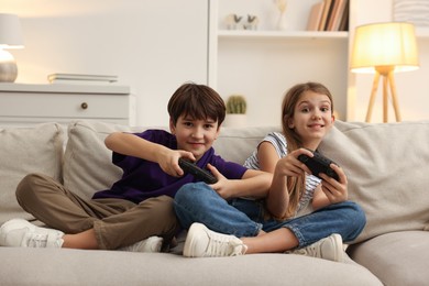 Photo of Cute kids playing video games on sofa in living room