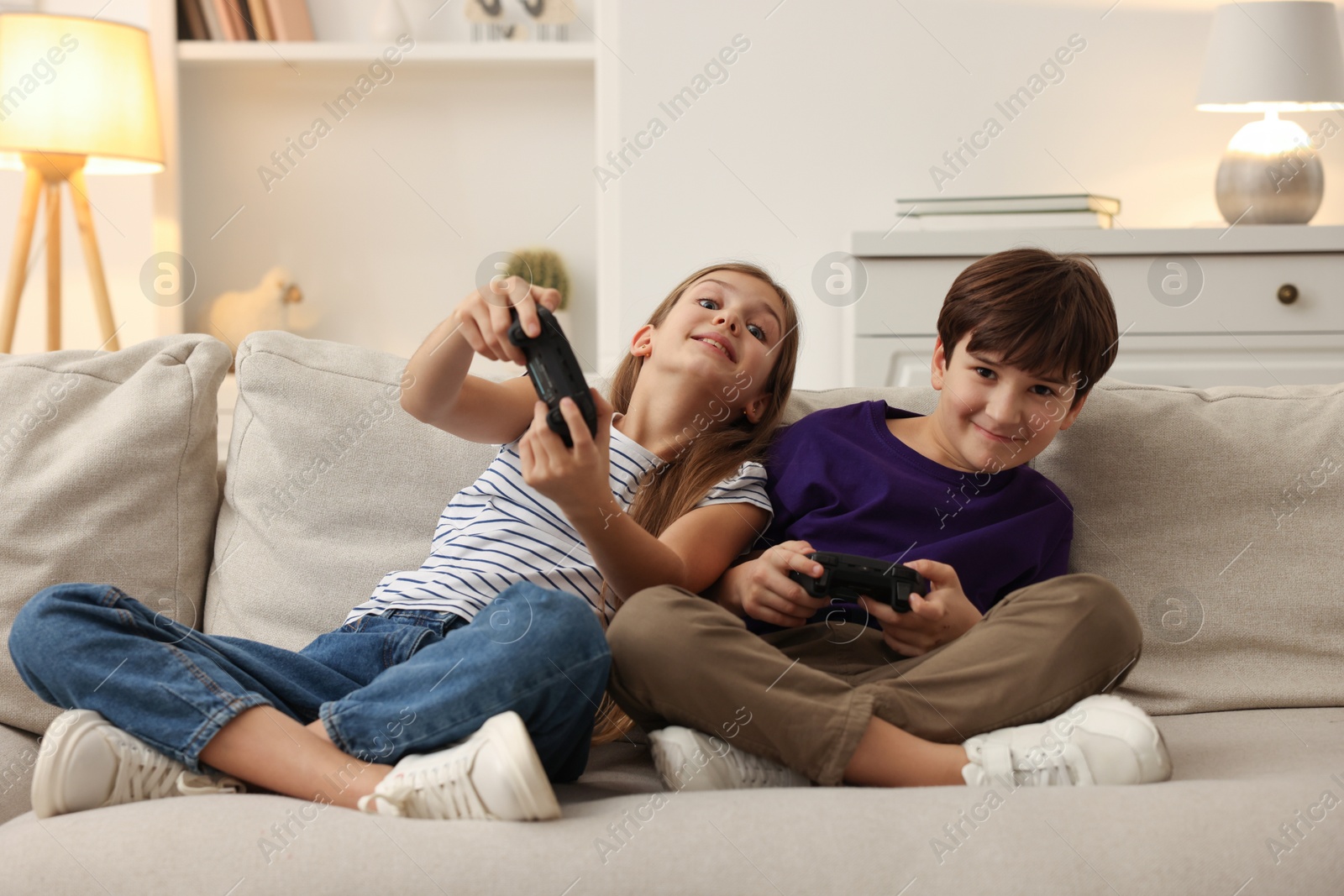 Photo of Cute kids playing video games on sofa in living room