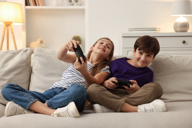 Photo of Cute kids playing video games on sofa in living room