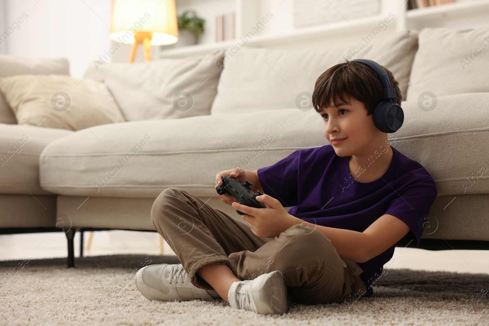 Photo of Cute boy in headphones playing video game on floor indoors