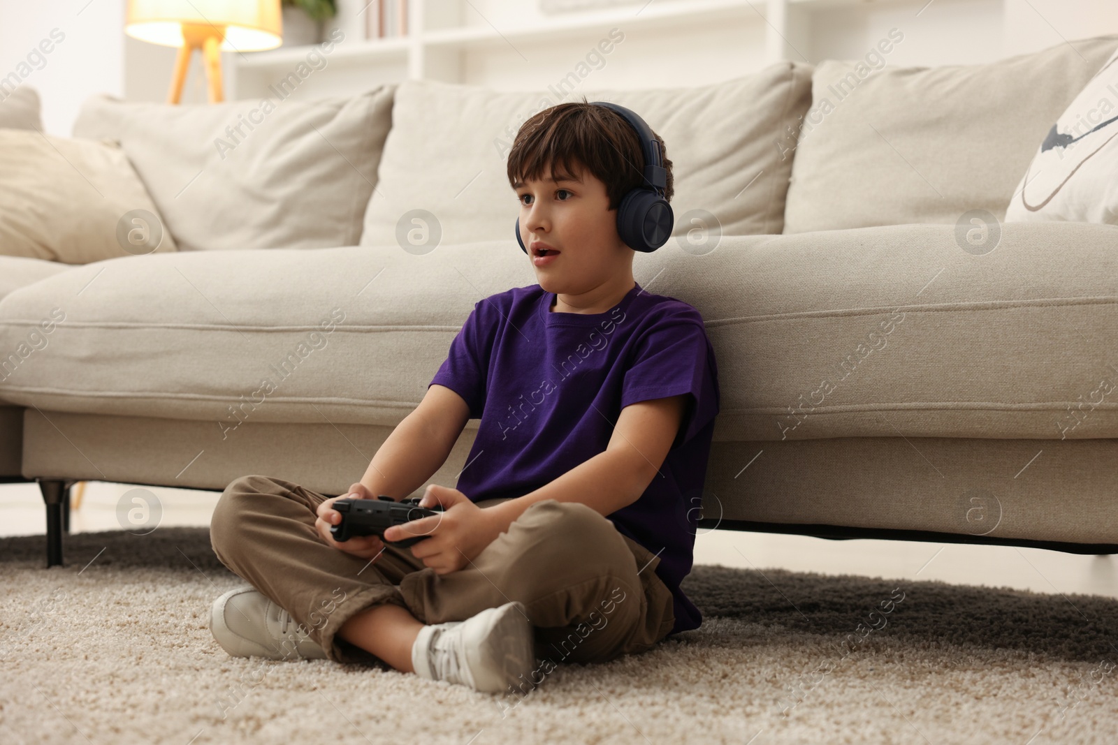 Photo of Cute boy in headphones playing video game on floor indoors