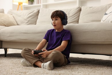 Photo of Cute boy in headphones playing video game on floor indoors