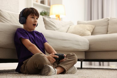 Photo of Cute boy in headphones playing video game on floor indoors