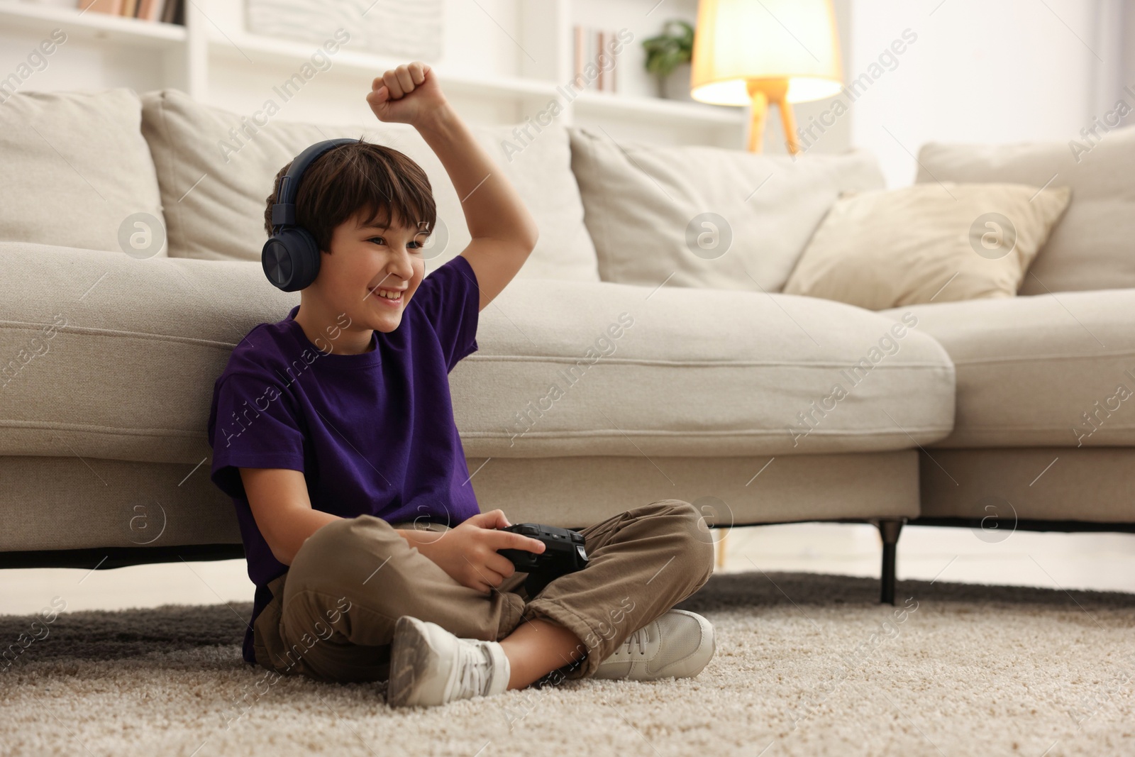 Photo of Cute boy in headphones playing video game on floor indoors