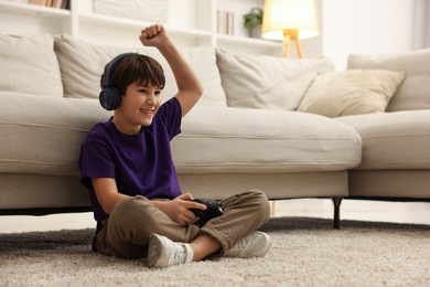 Photo of Cute boy in headphones playing video game on floor indoors