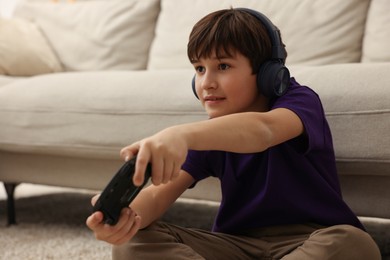 Photo of Cute boy in headphones playing video game on floor indoors