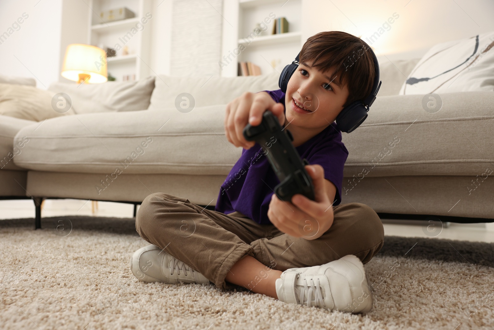 Photo of Cute boy in headphones playing video game on floor indoors