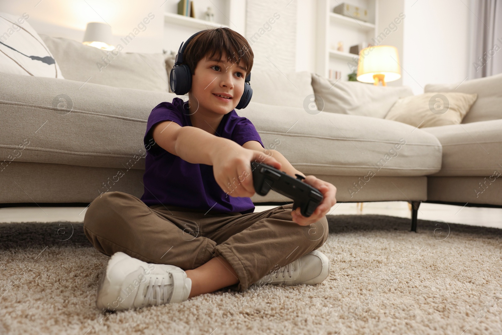 Photo of Cute boy in headphones playing video game on floor indoors