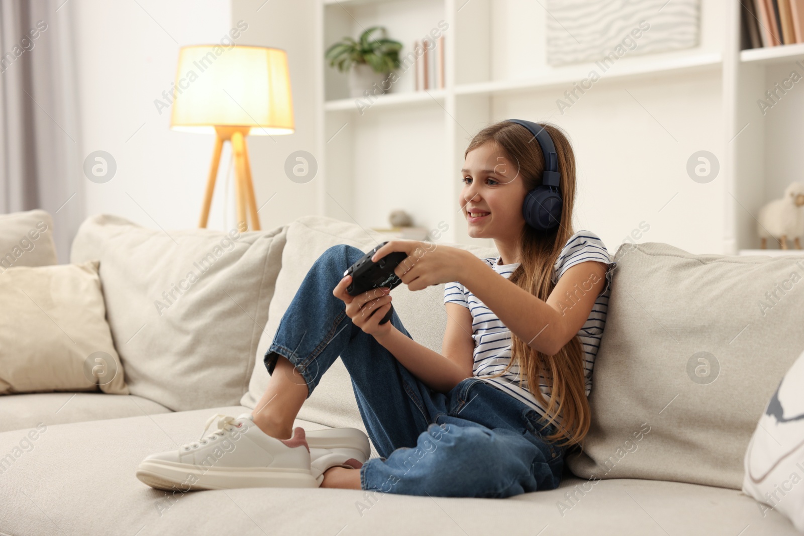 Photo of Cute girl in headphones playing video game on sofa at home