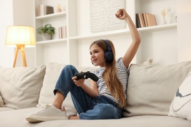 Photo of Cute girl in headphones playing video game on sofa at home