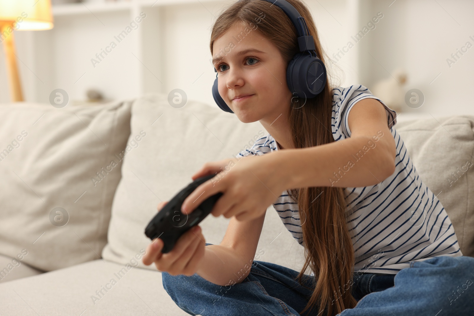 Photo of Cute girl in headphones playing video game on sofa at home