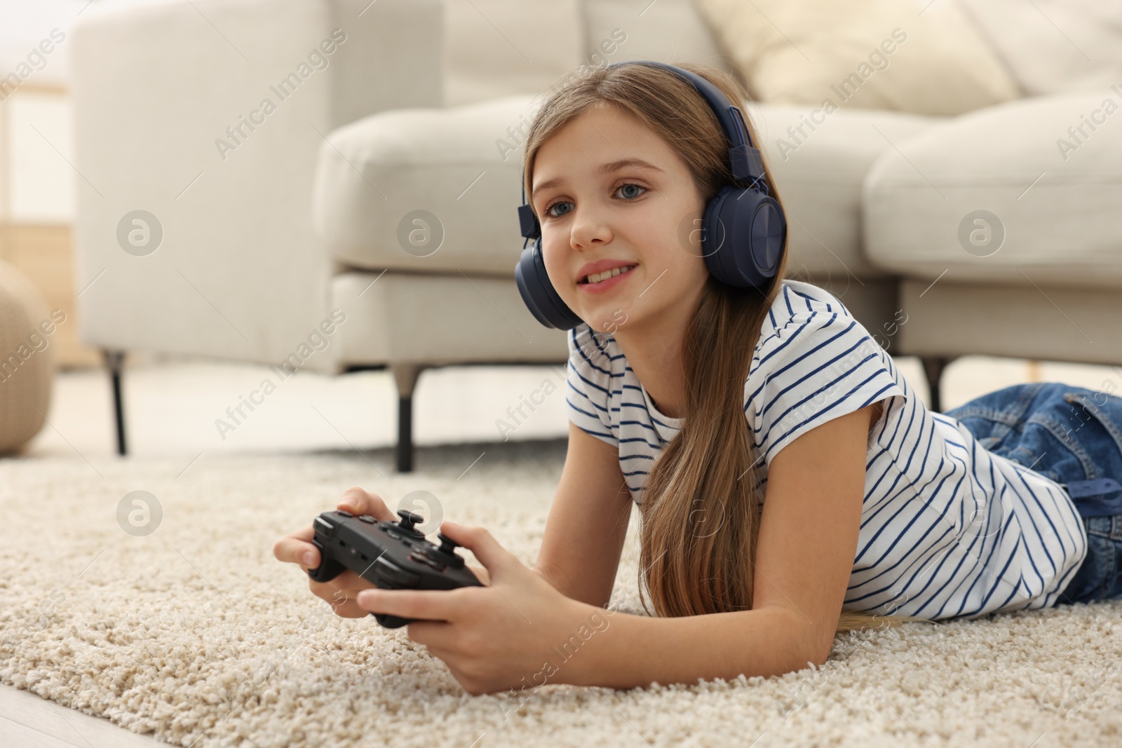 Photo of Happy girl in headphones playing video game on floor indoors, space for text