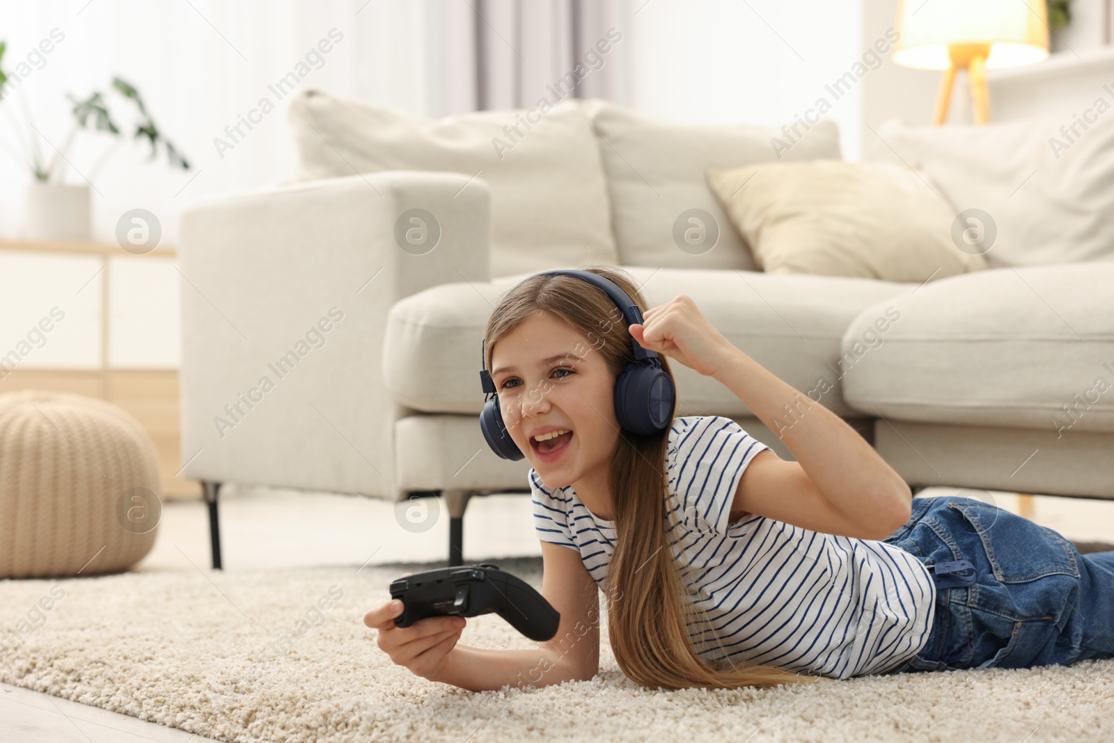 Photo of Happy girl in headphones playing video game on floor indoors, space for text