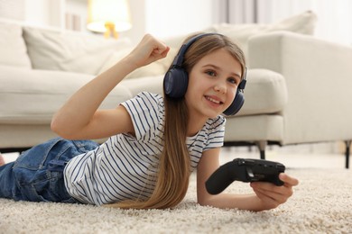 Photo of Happy girl in headphones playing video game on floor indoors